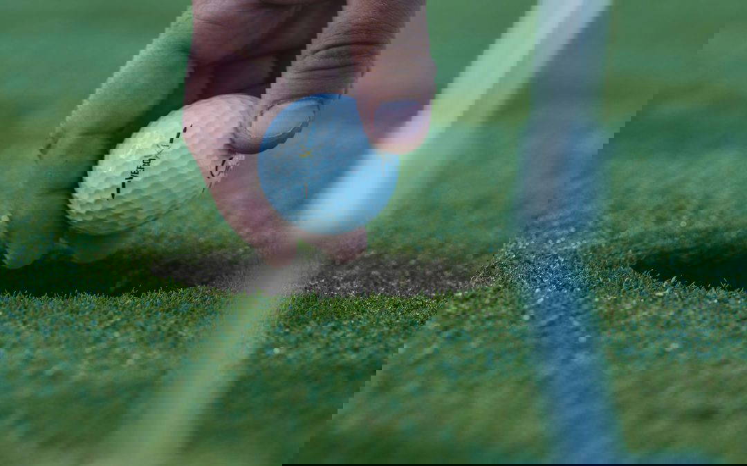 Hand placing a golf ball in the hole
